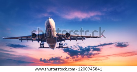 Landing airplane against colorful sky at sunset. Landscape with aircraft is flying in the blue sky with orange and pink clouds. Travel background with passenger plane. Commercial airplane. Private jet