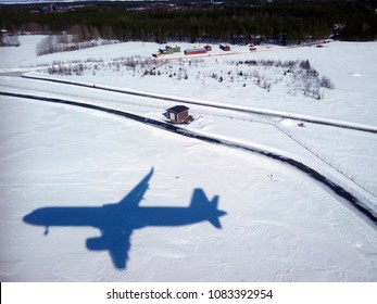 Landing In Oulu, Northern Ostrobothnia, Finland. The Shadow Of The Plane Against A Snow Covered Field With Houses And Forests In The Background.