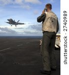 A Landing Signal Officer guides an F-18 Super Hornet aboard an aircraft carrier