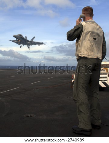 A Landing Signal Officer guides an F-18 Super Hornet aboard an aircraft carrier
