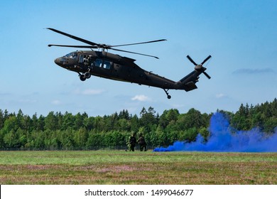 Landing of swedish military helicopter. Swedish Air Force. Military armed men with smoke bomb near forest under blue sky