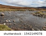 A landscacpe image of a wide shallow river that has to be crossed along Glen Geldie.  Rocks are strewn throughout the gently flowing water.