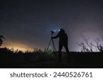 Landscape astrophotographer with a camera on a tripod outdoors in early spring at night under the starry sky. 