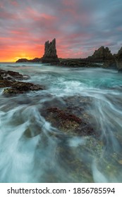 Landscape Of A Beautiful Rock. Waves Of The Ocean Surround Rocks. The Sky Catches Pre Dawn Lights Of The Rising Sun.