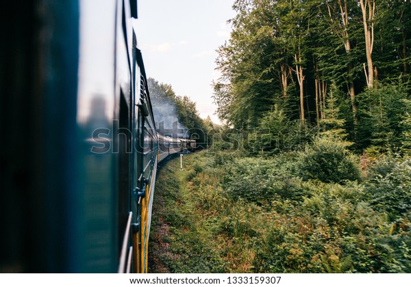Landscape beautiful view out of window from riding\
train among summer nature with hills, mountains and forest.\
Vacation and travel concept. Locomotive with train cars moving\
along railroad track