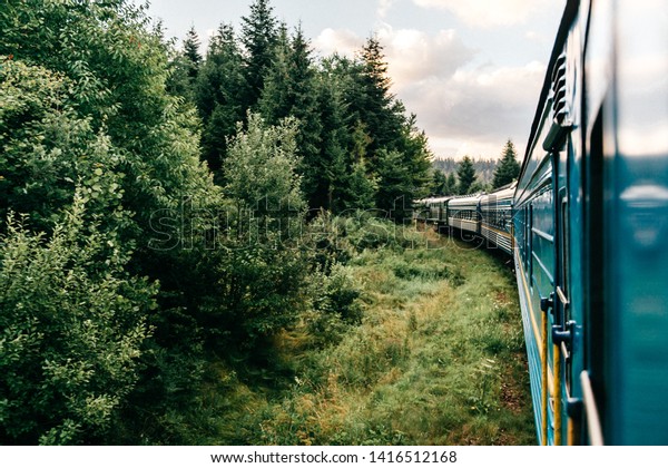 Landscape beautiful view out of window from riding\
train among summer nature with hills, mountains and forest.\
Vacation and travel concept. Locomotive with train cars moving\
along railroad track