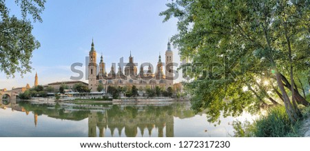 A landscape of christian Pilar Cathedral and Santiago Bridge reflecting in the Ebro river during a sunny summer day in Zaragoza, Aragon region, Spain