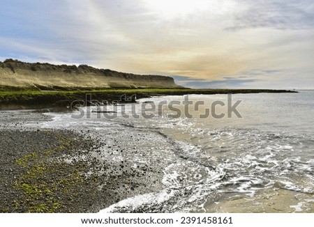 landscape of cliffs and plateasus with caverns and beaches of rocks, sand and moss, calm sea with foam and few waves washing the stony beach on a beautiful sunset