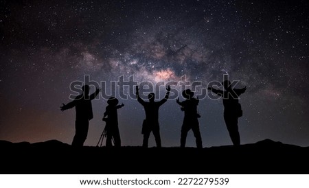 Landscape with colorful Milky Way and yellow light.Night starry sky with silhouette of photographer  happy people with raised-up arms on the rock. Beautiful Universe. Space background