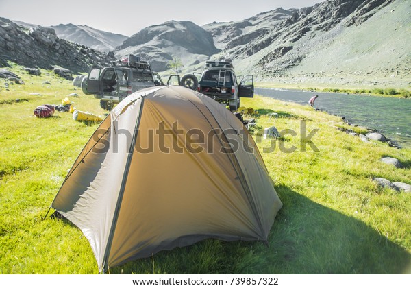 Landscape with colorful tourist\
tents on lakeside. Mongolia. People with car and tent at the\
campsite in grassland. The tourist camp in the mountains, tents and\
cars