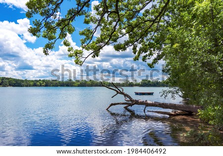 A landscape crop of a Wisconsin Lake (Lower Genesee Lake in Waukesha County).  A swimming raft floats on the calm waters while cumuls clouds are reflected.