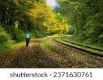 Landscape of a cyclist, seen from behind, on the Great Allegheny Passage Trail curving past railroad tracks and a forest on a moody early Autumn day.