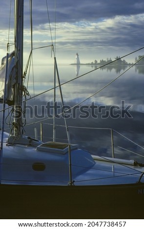 Landscape at dawn of lighthouse framed by sailboat rigging, Atlantic Ocean, Nova Scotia, Canada
