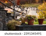 Landscape of decorative garden gnome dwarf with hat on the windowsill of a house on the green lawn among the Italian Alps Mountains in autumn with trees yellow and orange leaves in the background