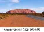 A landscape of a deserted valley at the highway road on the background of the Uluru