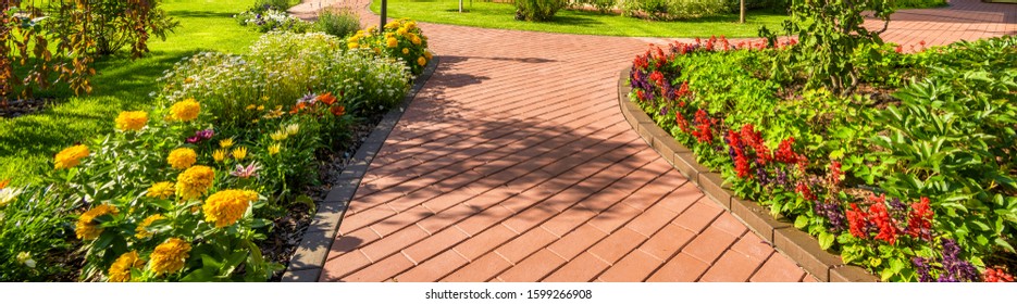 Landscape Design Of Backyard, Beautiful Lanscaping With Flower Beds In Summer. Panoramic View Of Walkway In Landscaped Yard. Scenery Of Tiled Way And Green Plants In Home Garden. Header, House Theme.