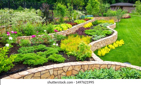 Landscape design of backyard, landscaping of upscale home garden. Scenic view of landscaped back yard of residential house with retaining walls, lawn and plants. Beautiful floral landscape in summer.