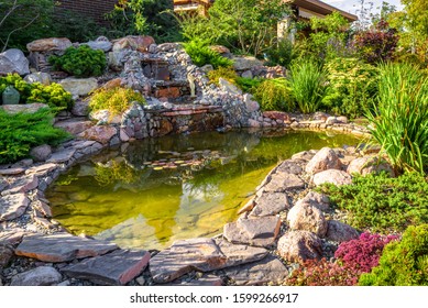 Landscape design in home garden, beautiful landscaping with small pond and waterfall. Landscaped place with stones and water at country house. Nice pond and fountain in backyard or yard in summer.