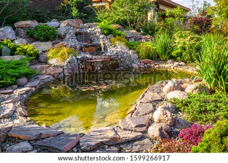 Landscape design in home garden, beautiful landscaping with small pond and waterfall. Landscaped place with stones and water at country house. Nice pond and fountain in backyard or yard in summer.