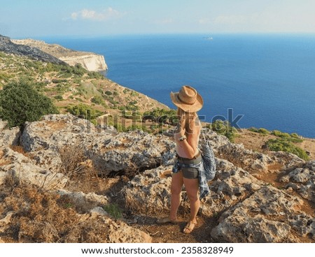 Landscape of Dingli cliffs edge Malta with blonde travel girl with straw cowboy hat and mediterranean sea coastline