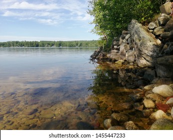 Landscape Of The Edge Of A Lake, With A Collection Of Large Stones And A Tree Overlooking The Water