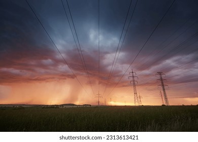 Landscape with electricity pylons under dramatic clouds of approaching rain with strong storm. Themes extreme weather, electrical energy and change climate.