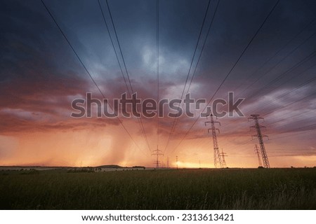 Landscape with electricity pylons under dramatic clouds of approaching rain with strong storm. Themes extreme weather, electrical energy and change climate.
