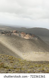 Landscape featuring a volcano to the foreground with another volcano in the background and a featureless blue grey sky. Portrait orientation.