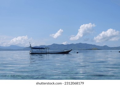landscape of a fishing boat in calm water with mountains and clouds behind at noon in the sea of ​​East Nusa Tenggara, Indonesia. - Shutterstock ID 2312068179