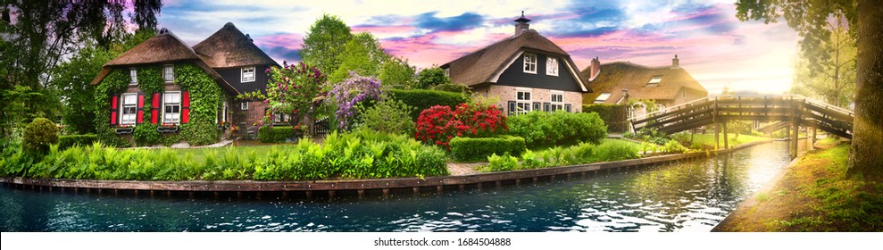 Landscape of Giethoorn village with water canals and rustic houses in netherland country wide banner or panorama. Old small brick house with thatched roof and wooden bridge. 