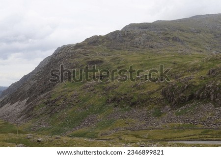 Landscape of a grassy hill dotted with rugged, weathered boulders under a clear blue sky.