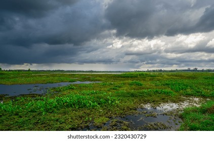 Landscape of green grass field and overcast sky. Dark cloudscape of a stormy sky. Natural water reservoir. Water sustainability. Freshwater for human consumption. Dark dramatic sky in the rainy season