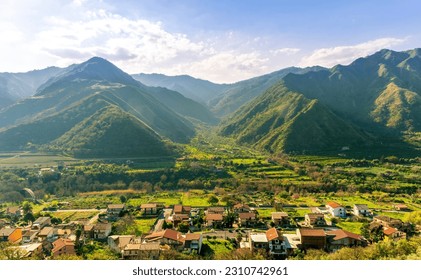 landscape of green summer highland mountain range with green beautiful valley with nice town below and amazing blue cloudy sky on background - Shutterstock ID 2310742961