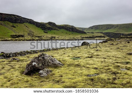 Landscape of Iceland in Kalfafell region with a river and stones in grass with overcast weather