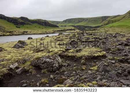 Landscape of Iceland in Kalfafell region with stones in grass, river and waterfall in the background