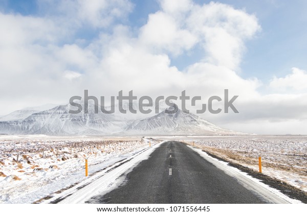 landscape of Iceland\'s golden\
circle road in winter.Asphalt road go straight to snow capped\
mountains.empty highway in countryside of iceland with volcano in\
background
