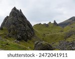 A landscape image of an ancient land with rolling green grassy hills between steep and craggy stacks of rock near the Old Man of Storr on Skye, Scotland.