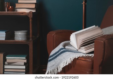 Landscape image of home interior. A book rests on a vintage old leather chair with books and objects seen on shelves in the background. Home office, cosy environment concept.