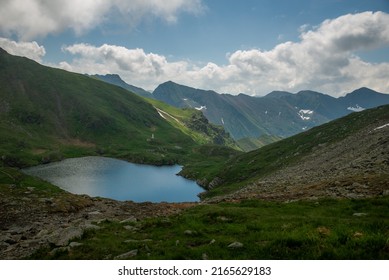 Landscape with impressive rocky mountains, green meadows, dramatic clouds, mountain lake and deep valleys. Located in Fagaras Natural Park, Transylvania, Romania.