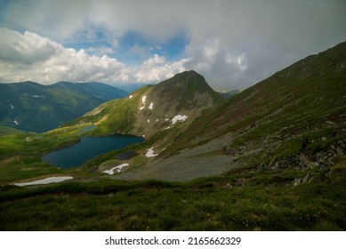 Landscape with impressive rocky mountains, green meadows, dramatic clouds, mountain lake, pink flowers and deep valleys. Located in Fagaras Natural Park, Transylvania, Romania.