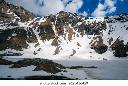 Landscape of Lacul Bâlea (Bâlea Lake) in the Făgăraș Mountains, Romania, during late winter or early spring. The frozen glacial lake is surrounded by rugged, snow-patched peaks and rustic mountain 