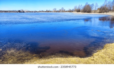 Landscape with a lake covered with ice before the start of melting and ice drift on spring day with the sun. Blue ice and water under sunlight in early spring or autumn