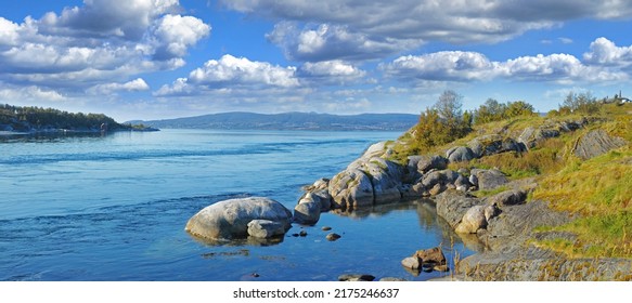 Landscape Of A Lake With A Rocky Shore On A Bright Cloudy Day. Green Hill With Boulders By The Seaside With A Blue Sky In Norway. A Calm Serene Horizon Of A Vibrant Peaceful Nature Scene In Nordland