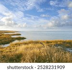 Landscape, lake and sky with clouds, nature and shoreline with grass bank, location and horizon in summer. Water, ground and outdoor in environment, sustainability and sunshine in wild in Denmark