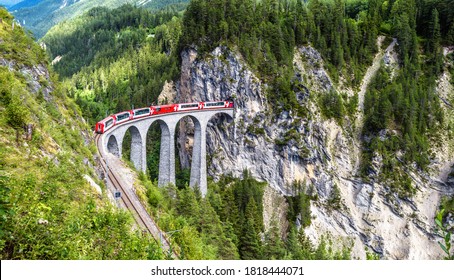 Landscape with Landwasser Viaduct in summer, Filisur, Switzerland. It is landmark of Swiss Alps. Panoramic view of railroad bridge and red train. Rhaetian glacier express runs on amazing railway. - Shutterstock ID 1818444071
