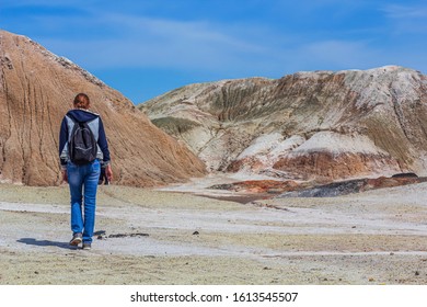 Landscape like a planet Mars surface. Young woman goes walks among the hills, view from the back. Solidified red-brown black Earth surface. Hiking concept. 