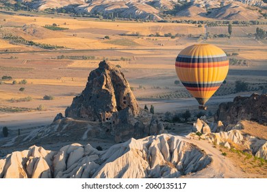 landscape with lonely hot air balloon with rainbow colors pattern rising over the Cappadocian valley panorama in the morning light with chimney rock houses in the foreground