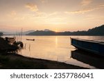The landscape of the Mekong River during sunset, traditional Laos ferry boats dock on the riverbank, and a fisherman rowing sampan on the river. Luang Prabang, Laos.