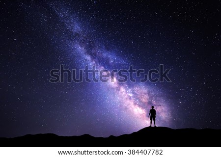 Landscape with Milky Way. Night sky with stars and silhouette of a standing happy man on the mountain.