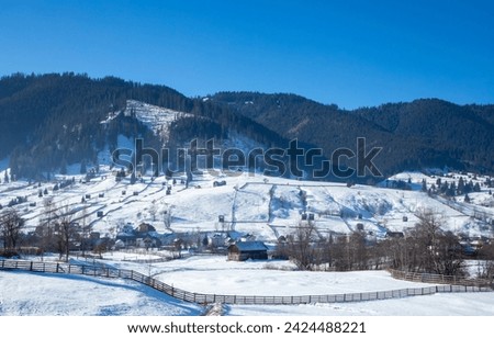 Landscape with a mountain village in winter. Houses spread out on a slope in the countryside covered with snow